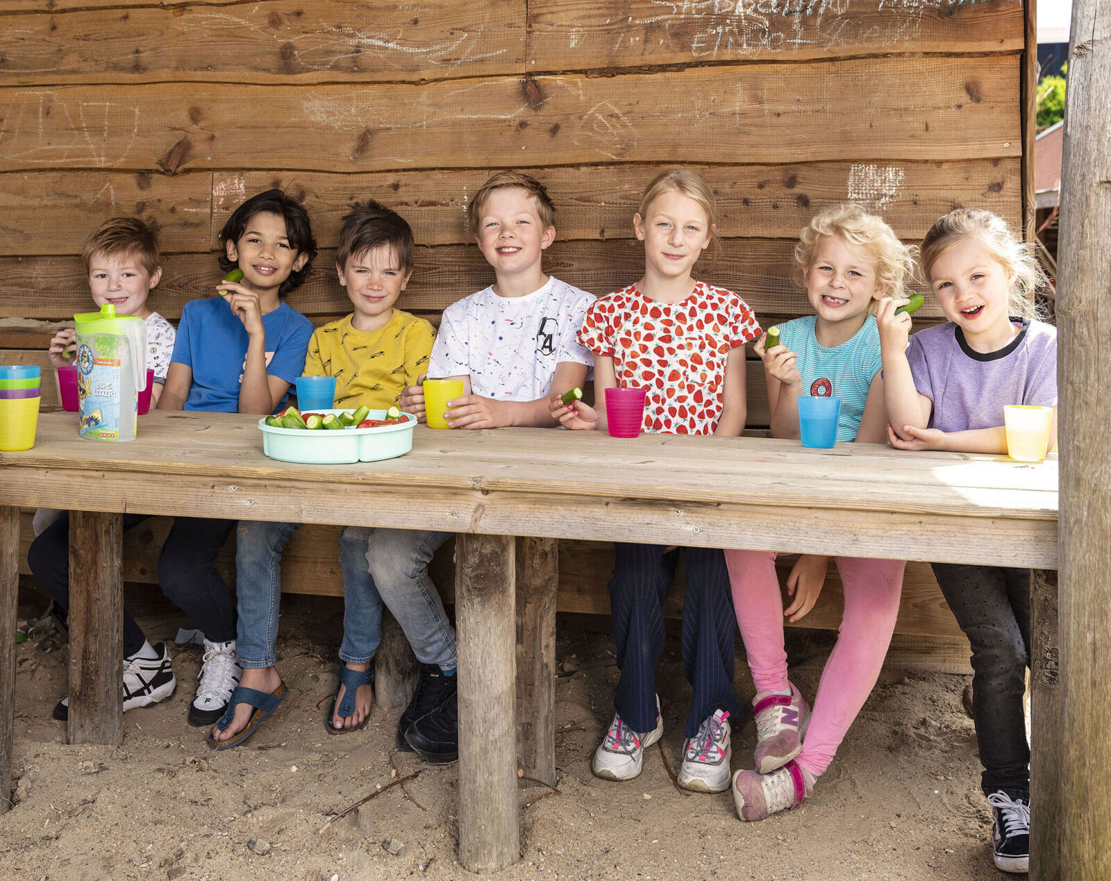 7 kinderen zitten op een bankje in de tuin van kinderdagopvang Yes!